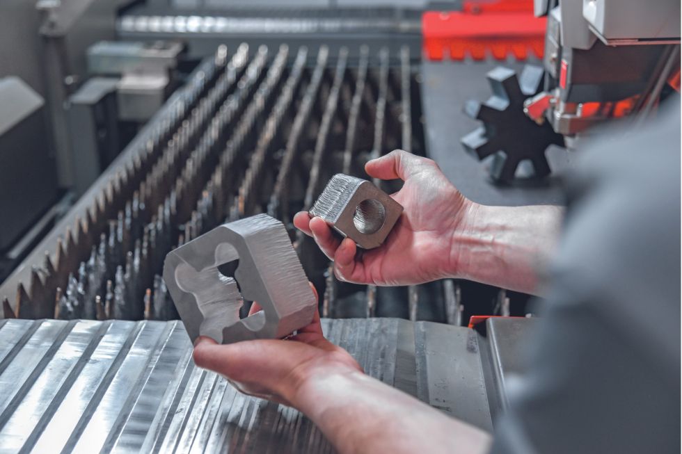 person holding two metal parts which were cut with a fiber laser