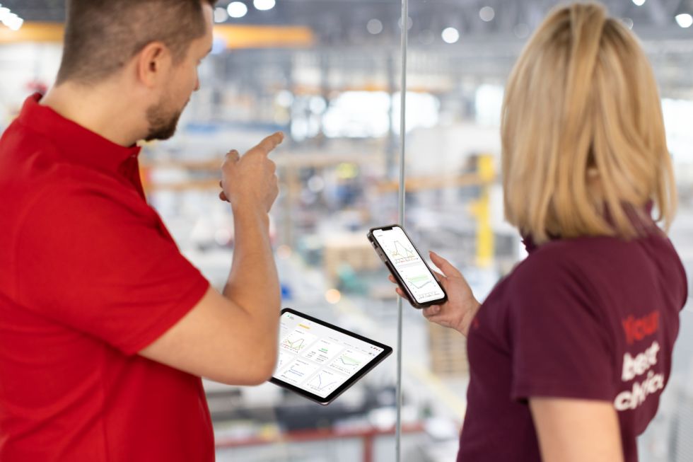 Two people looking at BySoft Insight on phone and table screens with factory/warehouse in the background